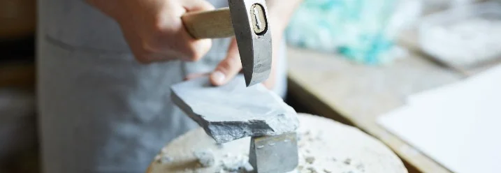 Person zerkleinert Stein mit Hammer